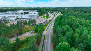 Ilmakuvassa Fazerilan alueen rakennuksia, läheistä puustoa ja metsää, ajorata ja kevyen liikenteen väylä.