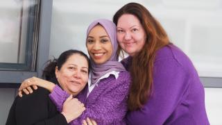 Neuvova Vantaa -hankkeen työntekijät Khalida, Mariam ja Irina hymyilevät kameralle toisiaan halaten.
