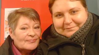 Anne ja Eeva mustat takit päällä punaisen taustaseinän edessä.