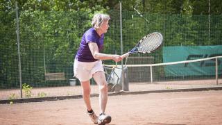 Shortseihin ja t-paitaan pukeutunut nainen juoksee tenniskentällä maila kädessä.