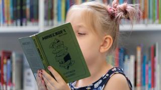 Ett barn läser en bok i bibliotek.