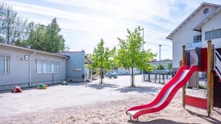Itä-Hakkilan koulun piha: liukumäki, koulurakennuksia ja kesäisiä puita.