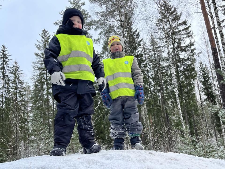 Kaksi lasta on kiivennyt suuren kiven päälle ja hymyilee kivellä seisten.